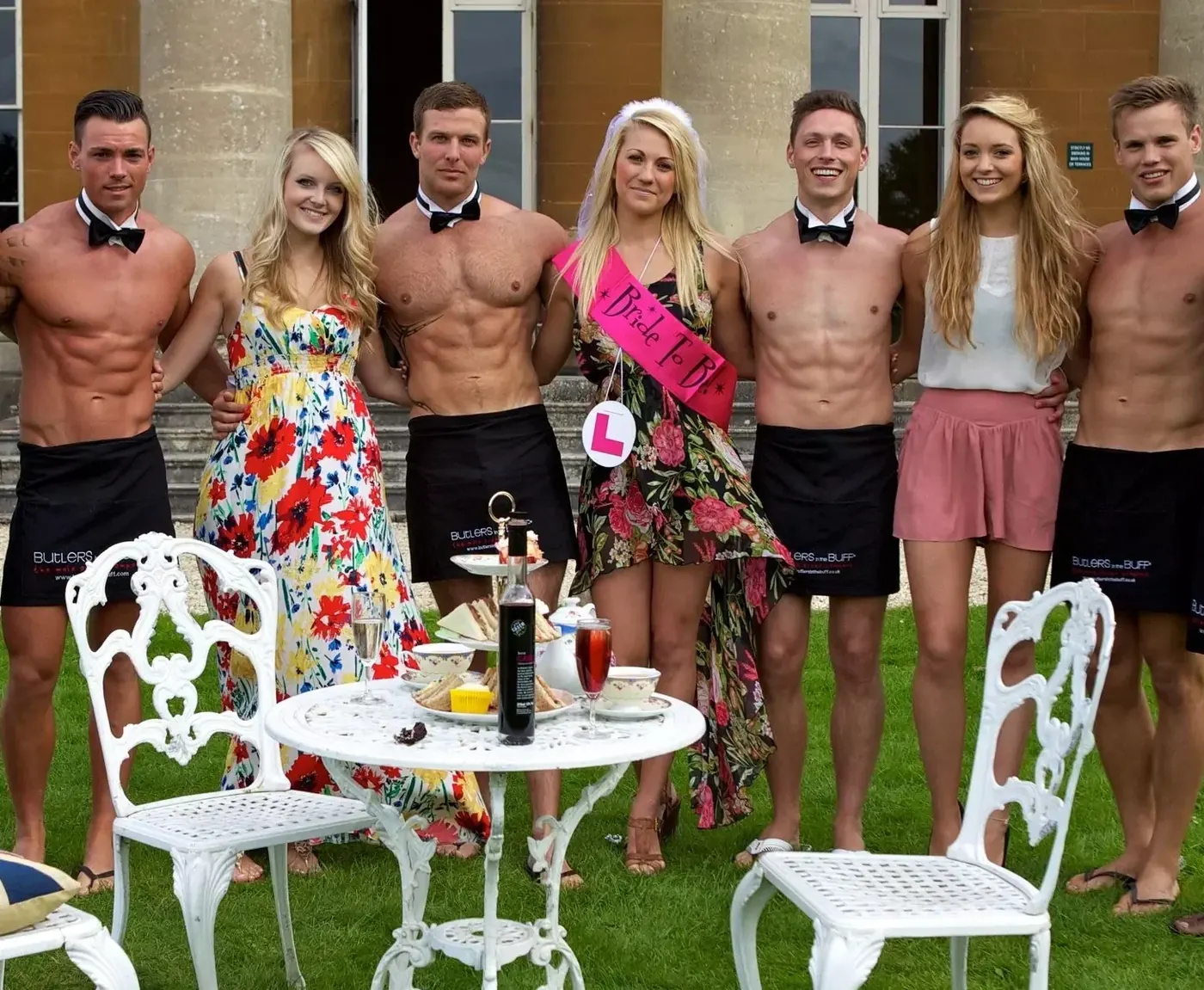 Five Butlers in the Buff in bow ties and aprons with a bride-to-be and friends at a garden afternoon tea