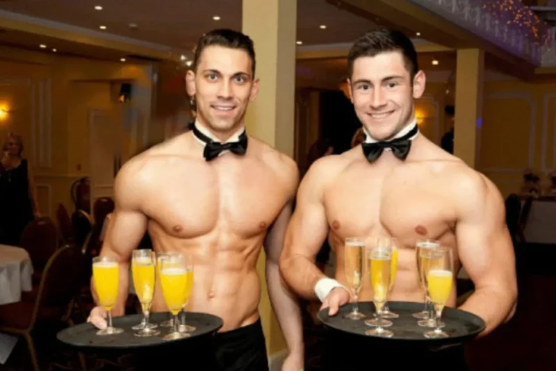 Two Butlers in the Buff serving trays of mimosas and champagne