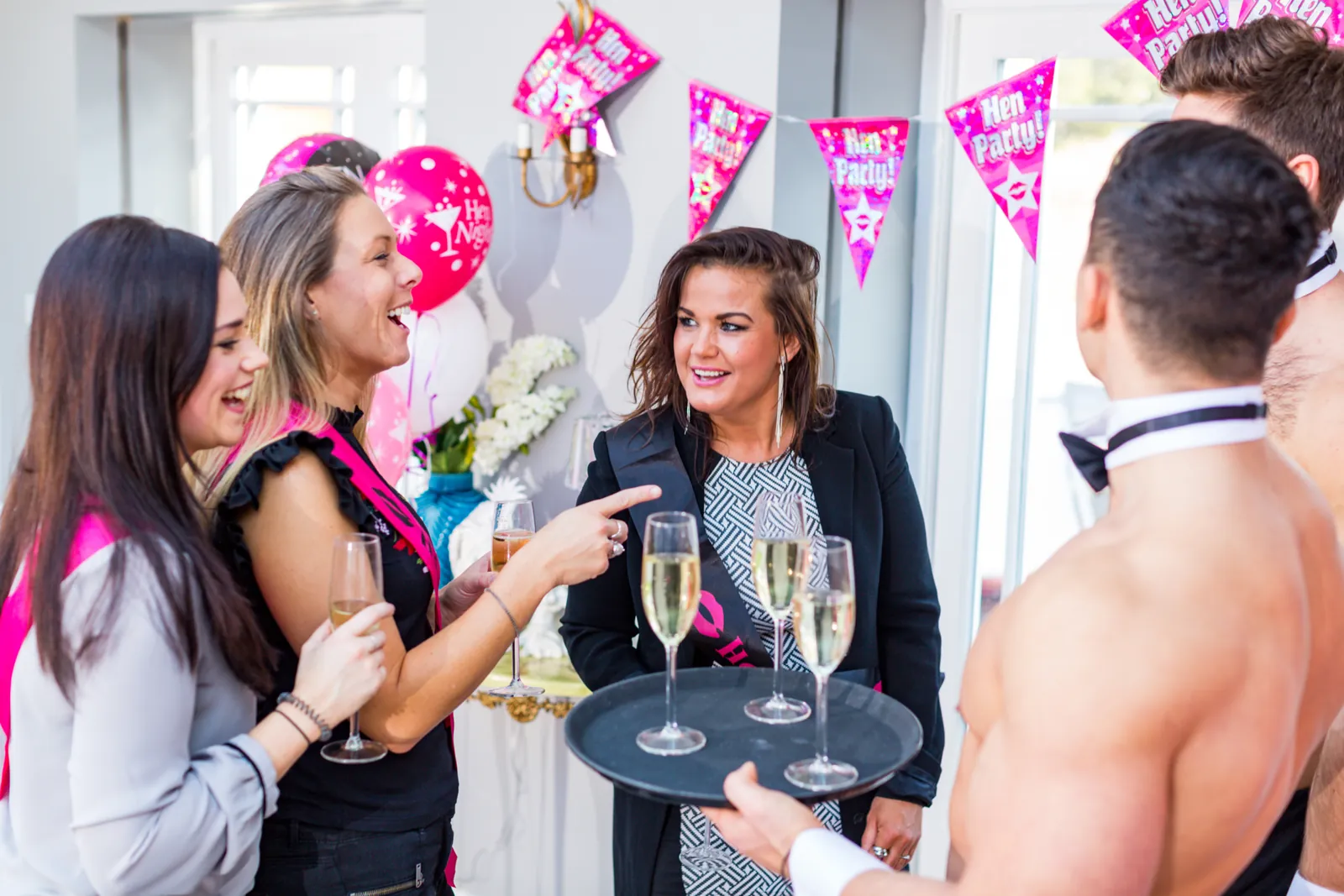 A Butler in the Buff serving champagne from a tray to a group of women at a hens party