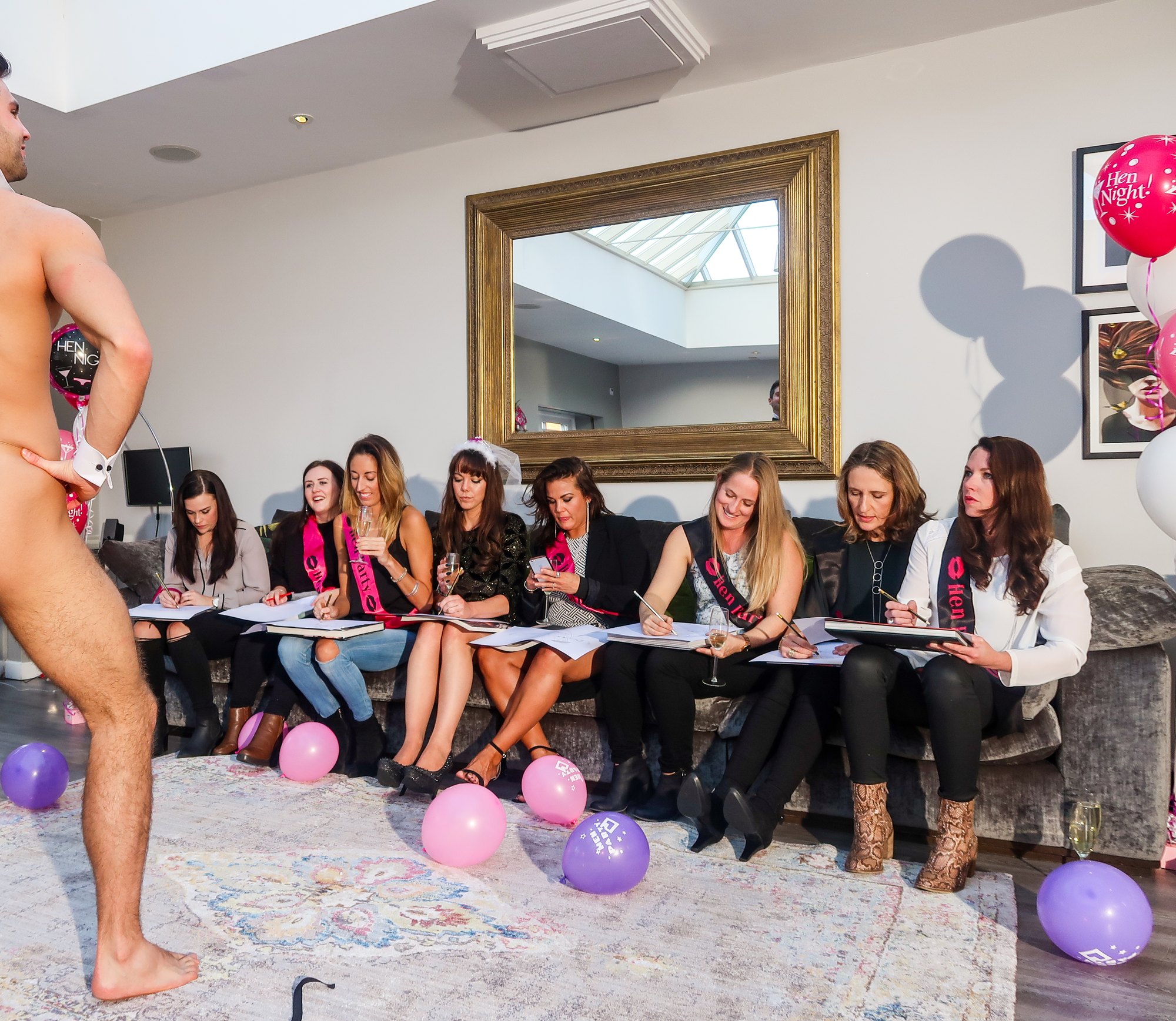 Hens party guests sketching on a sofa during a life drawing class with balloons